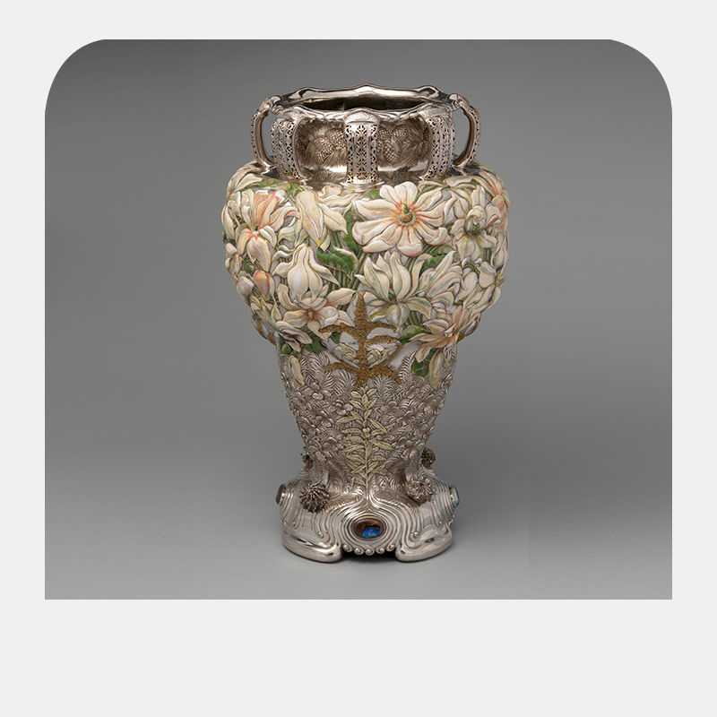 A silver vase with ornamented pale flowers etched at the neck.